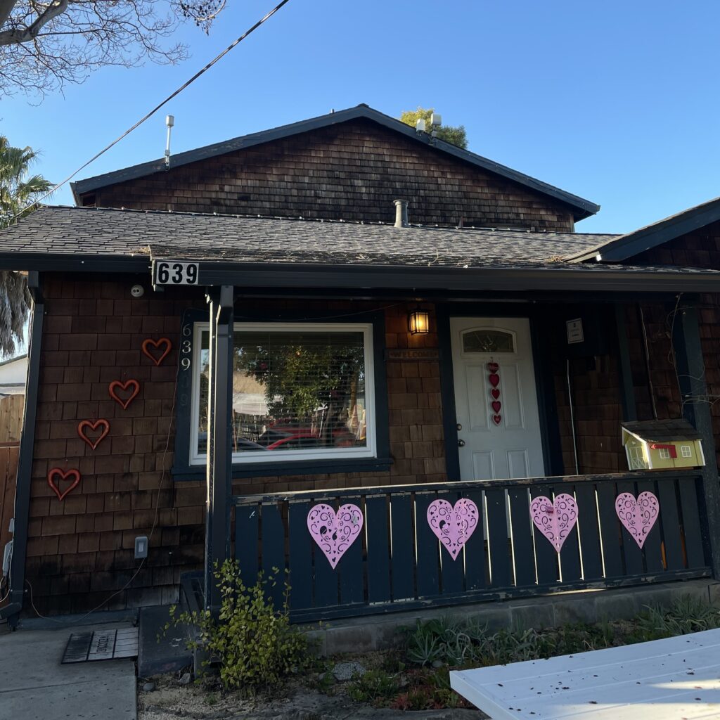 A brown house with a blue railing that features pink paper hearts hanging from it.