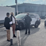 Women standing with man next to police vehicle.